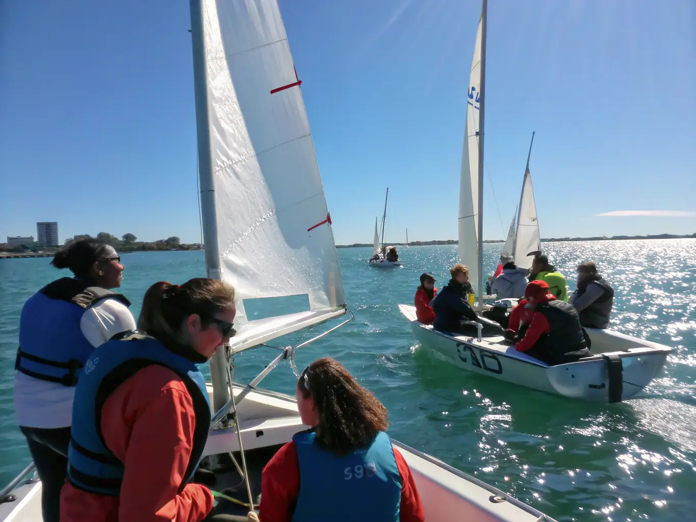 A dynamic image showcasing a group of children participating in a beginner sailing lesson, with instructors nearby, on a sunny day at Lion-sur-Mer.